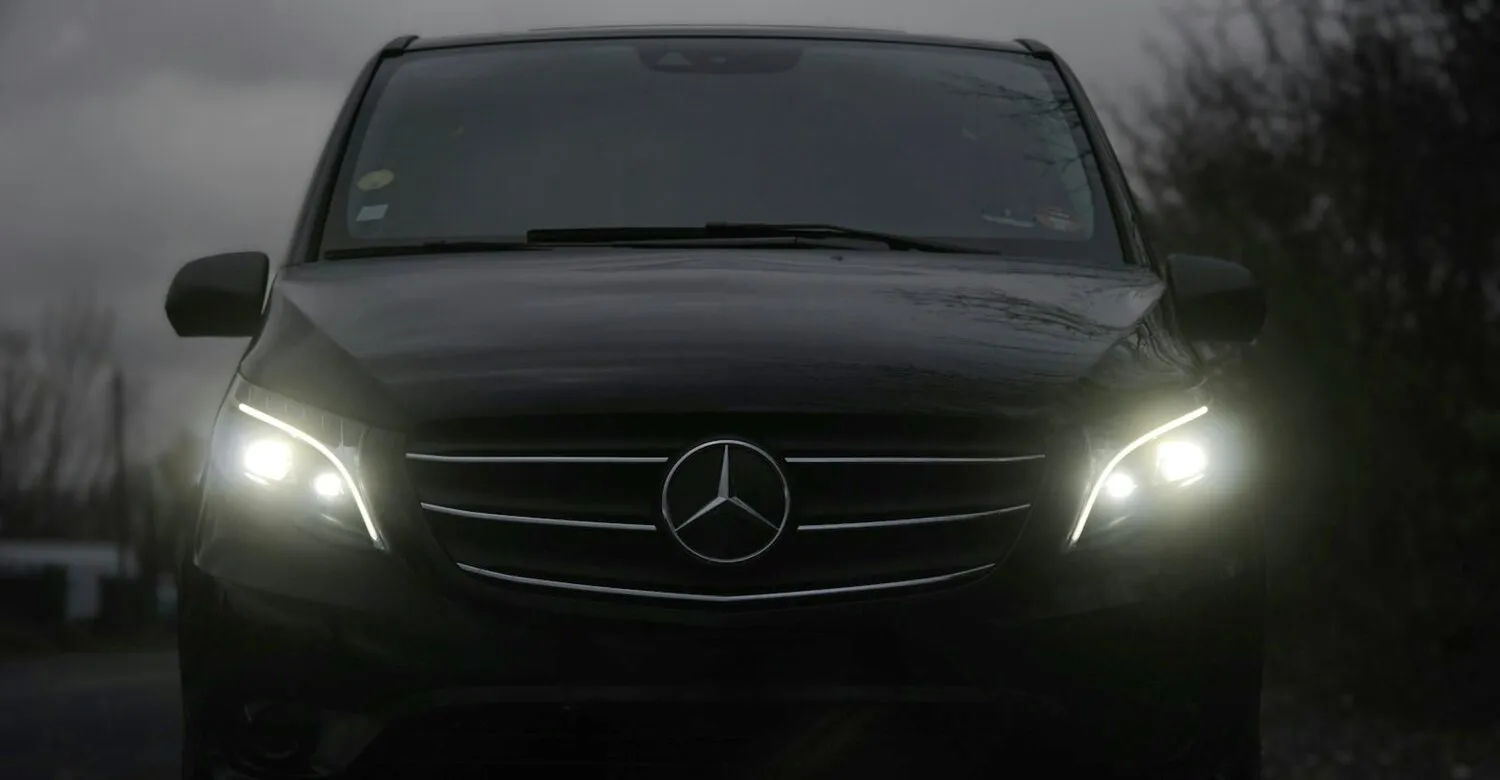 Microbuz Mercedes Vito negru, văzut din față, cu farurile aprinse